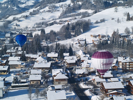 Le village de Praz-sur-Arly sous la neige, survolé par des montgolfières