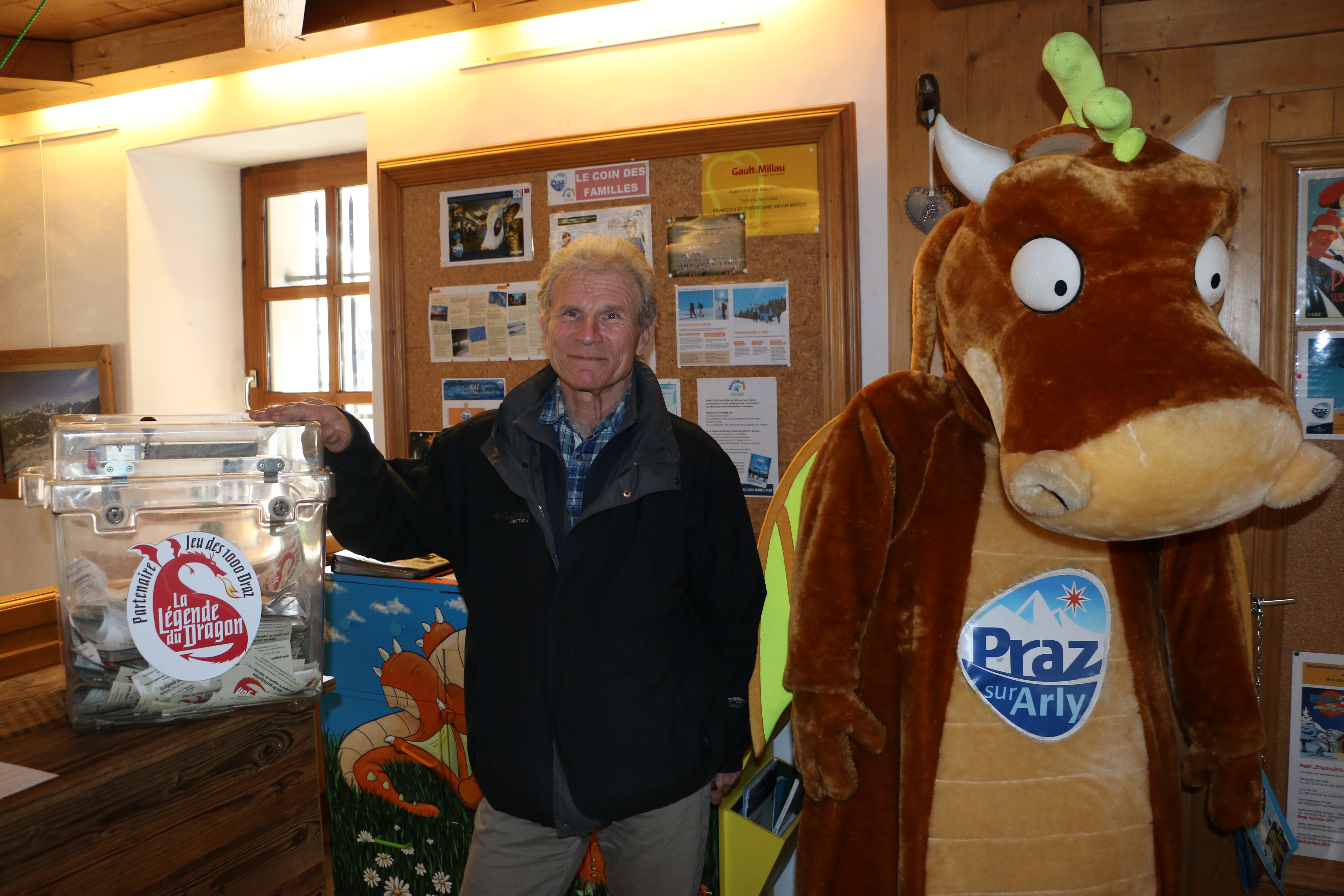 Alain Gac pose devant l'urne, à l'office de tourisme, où le public peut déposer les tickets reçus auprès des entreprises participant au Jeu des 1 000 Draz. À ses côtés, la mascotte Draz - Yann Jaccaz