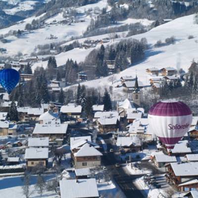 Le village de Praz-sur-Arly sous la neige, survolé par des montgolfières